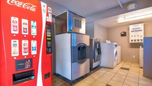 A hotel room with a Coca-Cola vending machine, a refrigerator, a washing machine, and a sign for soap and bleach softeners. - Motel 6 Rolling Meadows, IL - Chicago Northwest (Rolling Meadows)
