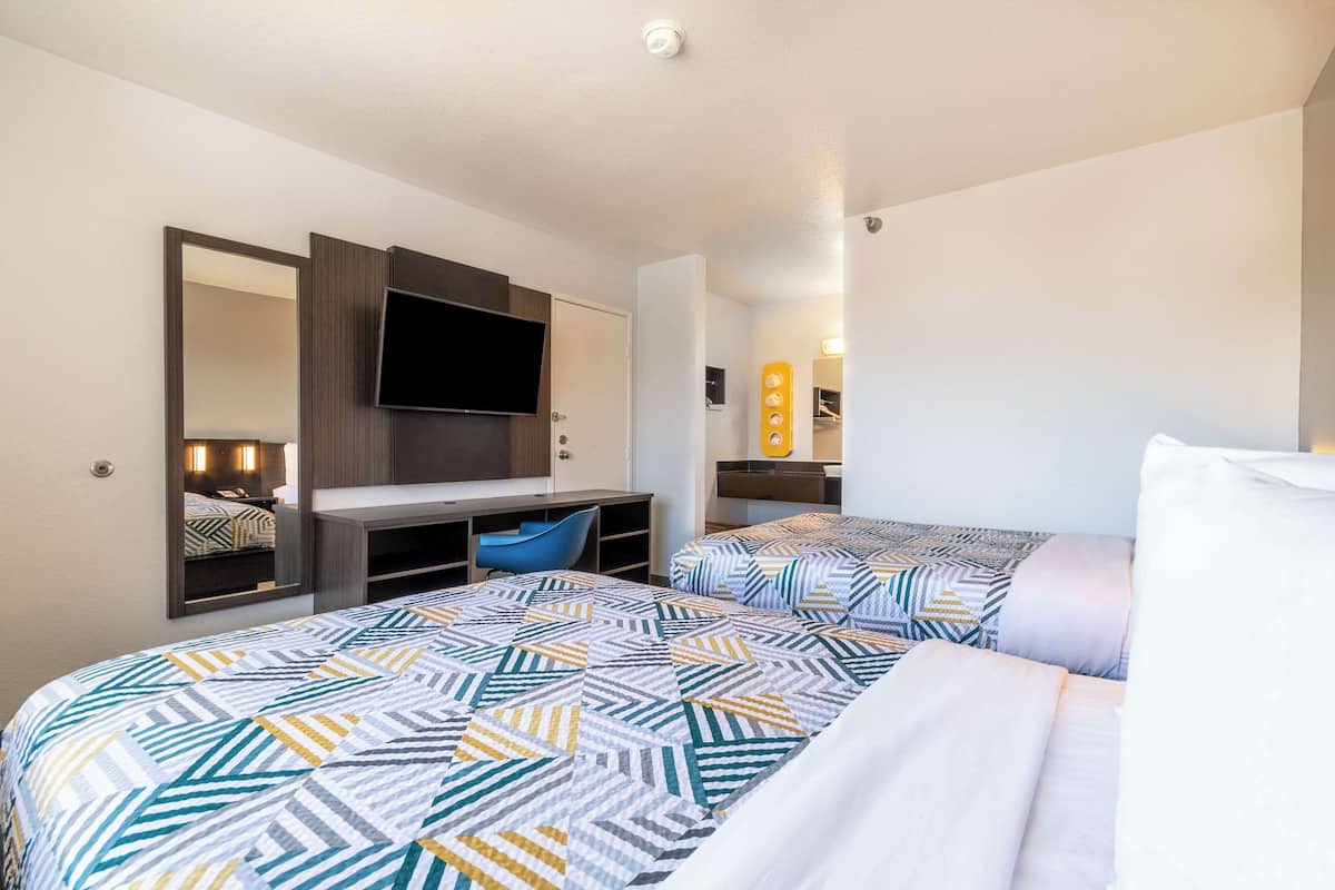 A hotel room with two beds, a TV, a desk, and a mirror.