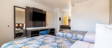 A hotel room with two beds, a TV, a desk, and a mirror.