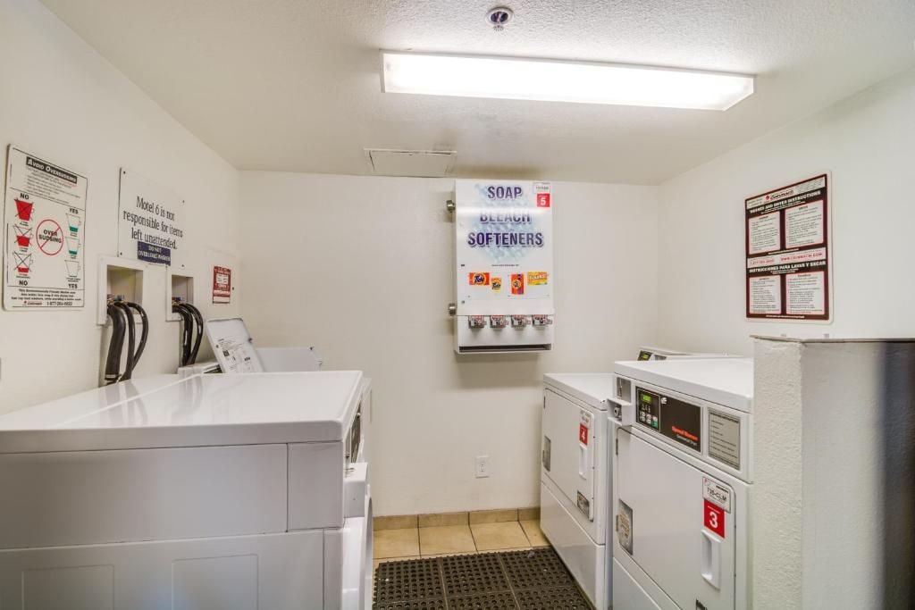 A laundry room with white appliances, a soap and bleach sign, and safety instructions on the walls.