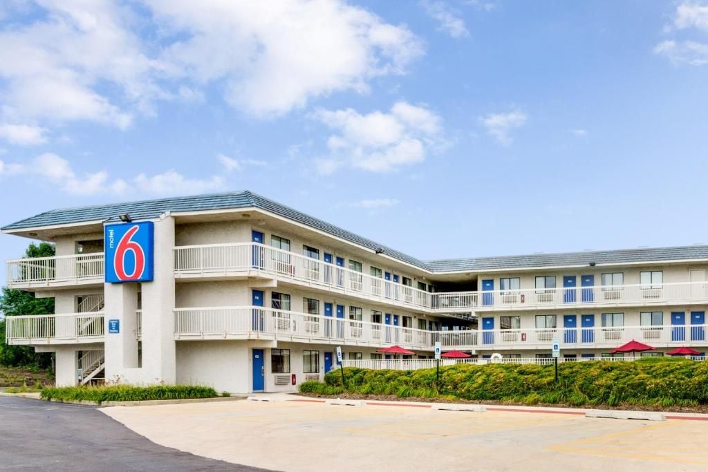 Een motel met meerdere verdiepingen, een groot bord met het cijfer '6', balkons en een parkeerplaats.