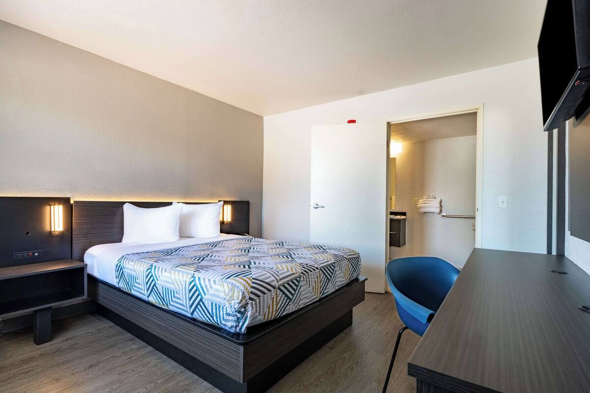 A hotel room with a bed, bedside table, chair, desk, and a television.