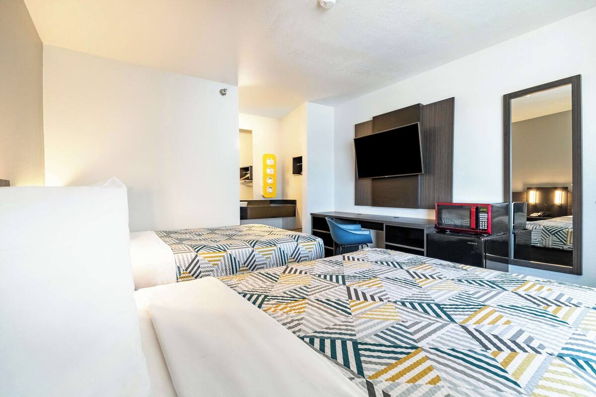 A hotel room with two beds, a desk with a TV, a microwave, and a mirror.