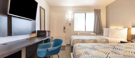 Ett hotellrum med ett skrivbord, en tv, en säng med mönstrat sänglinne, ett fönster med gardiner och en sänglampa.