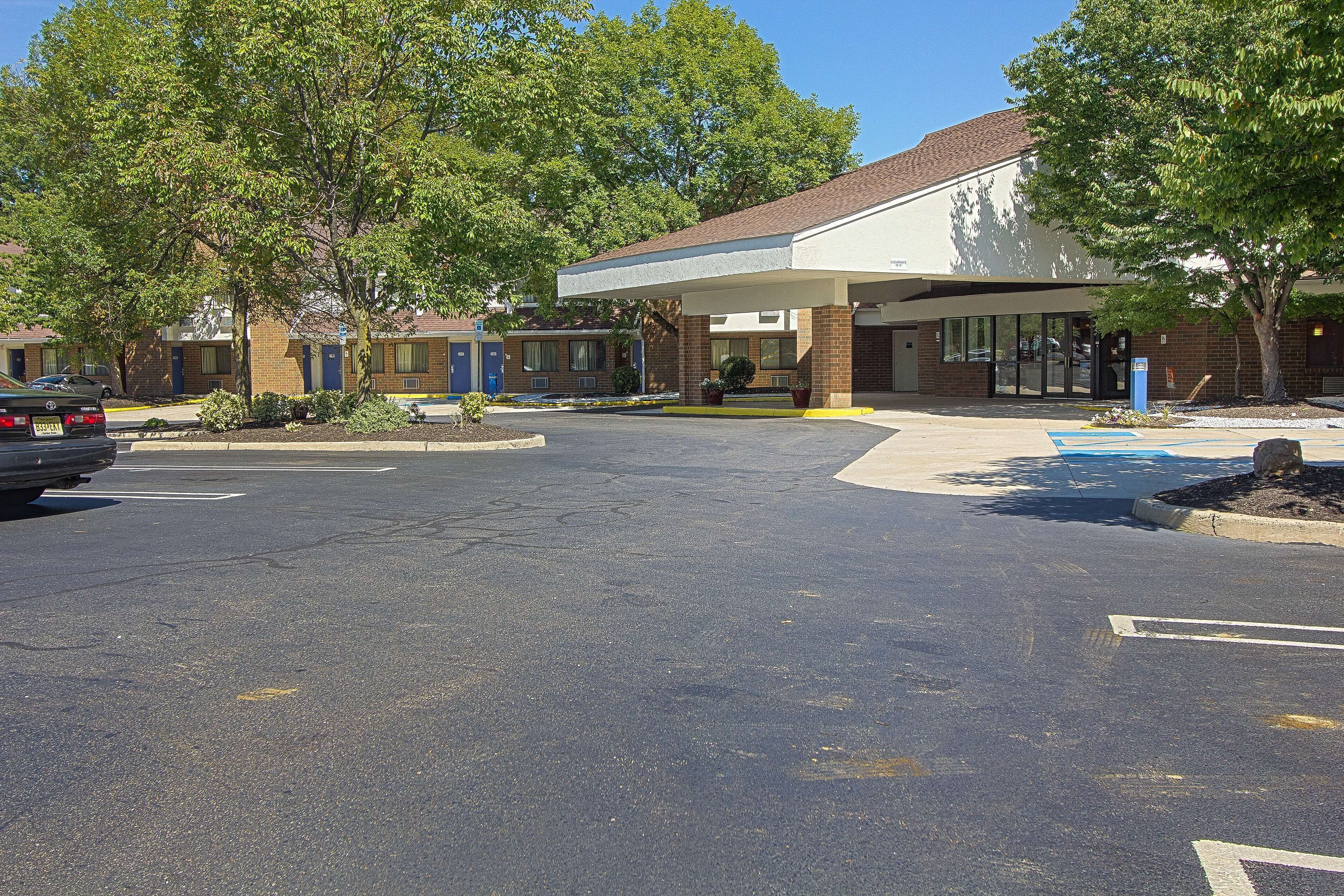 A motel with a covered parking area, a brick building, and a large tree in front.