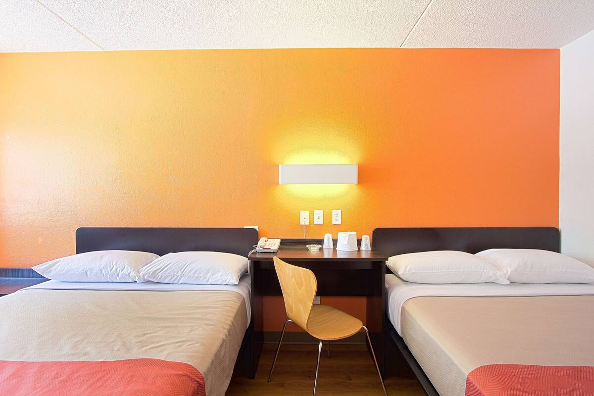 Habitación de hotel con dos camas, un escritorio, una silla y una lámpara fijada a la pared.