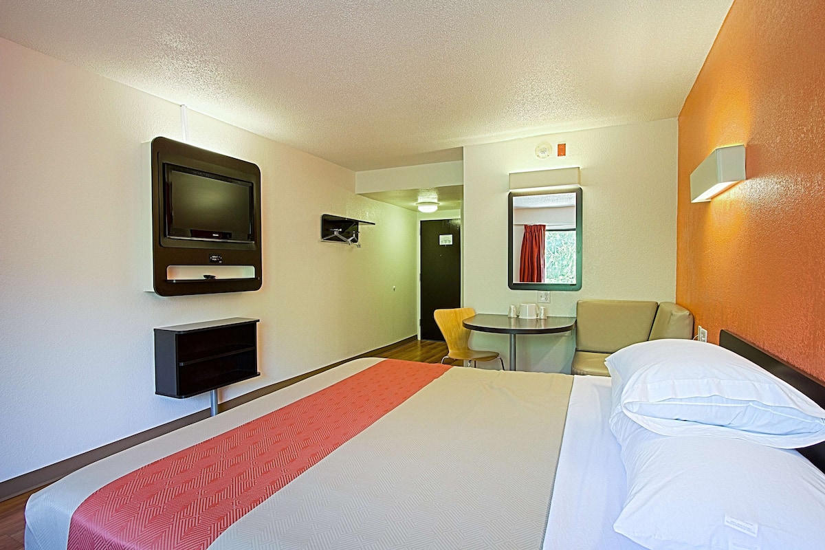 Una habitación de hotel con una cama, televisión, una mesita y una silla.