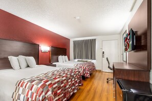 A hotel room with two beds, a desk, a TV, and a window with curtains.