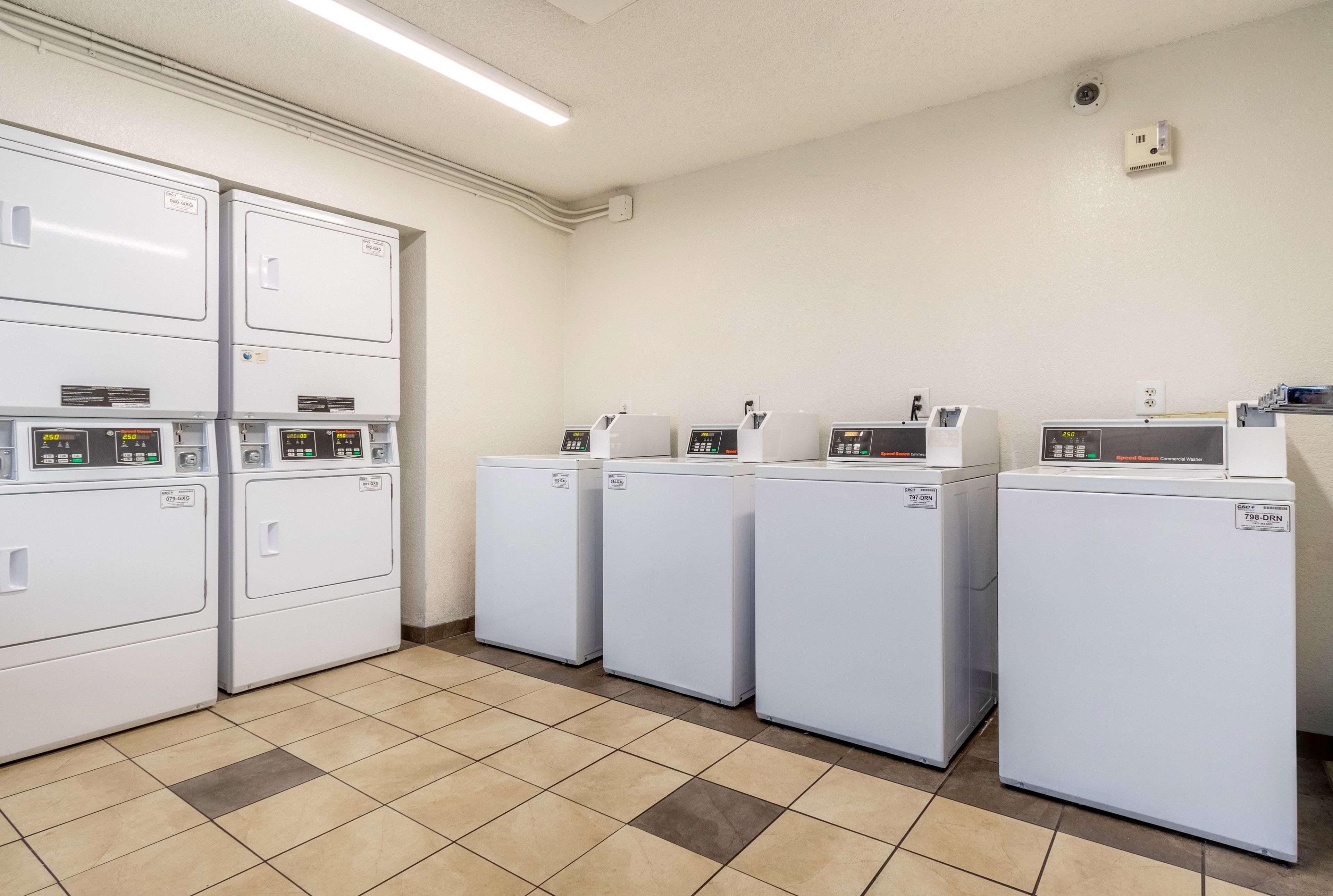 A laundry facility with multiple washing machines and dryers, a tiled floor, and a ceiling light.