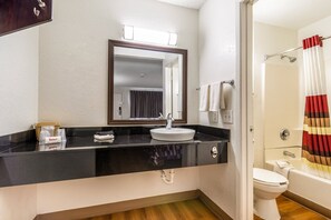 A bathroom with a black countertop, white sink, and a mirror above it. There is a shower curtain with a striped pattern and a white toilet.