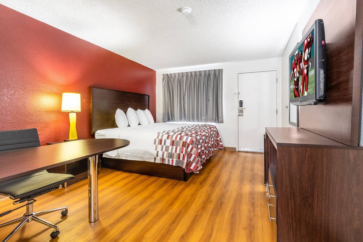 A hotel room with a bed, a desk, a lamp, a TV, and a wardrobe.