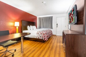 A hotel room with a bed, a desk, a lamp, a TV, and a wardrobe.