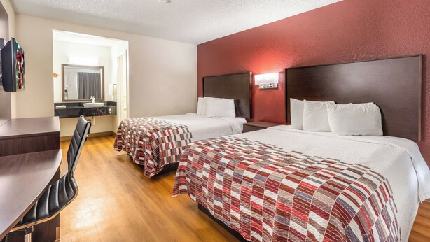 A hotel room with two beds, a desk, a chair, a mirror, and a red accent wall. - Red Roof Inn Phoenix - Midtown (Phoenix)