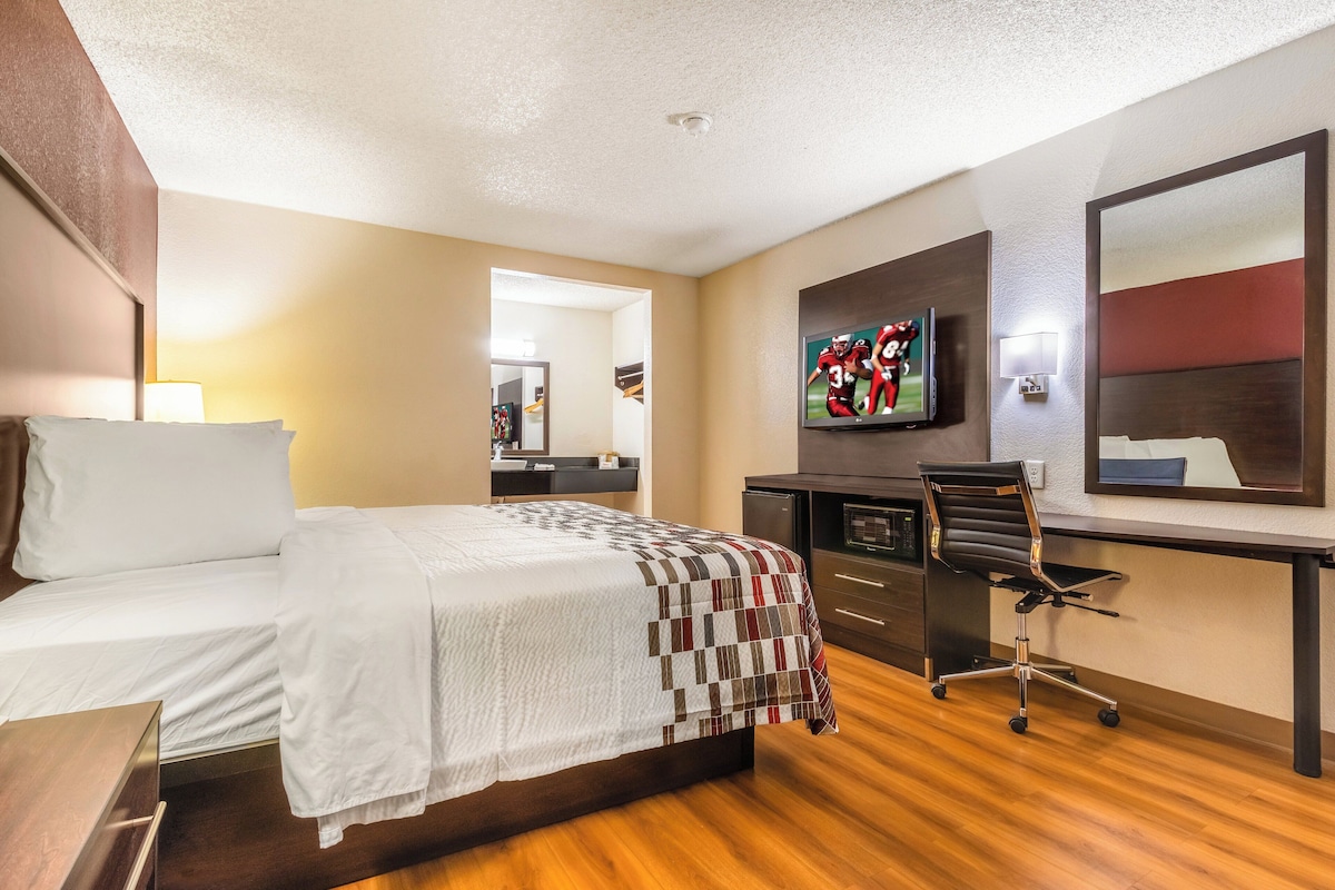 A hotel room with a bed, desk, chair, television, and a mirror.