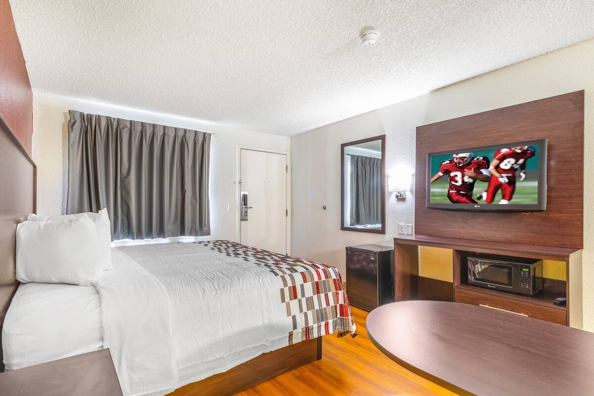 A hotel room with a bed, a TV mounted on the wall, a microwave, and a small cabinet.