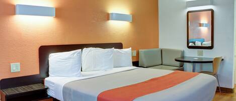 A hotel room with a large bed, a desk, and a chair. There are wall-mounted lights and a mirror above the desk.