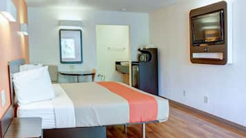 Una habitación de hotel con una cama, un escritorio, una mesita pequeña, un microondas y un televisor montado en la pared.