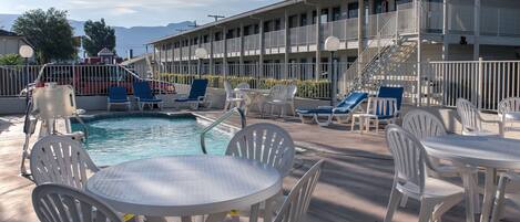 A pool area with lounge chairs and tables, a swimming pool, and a building with balconies.