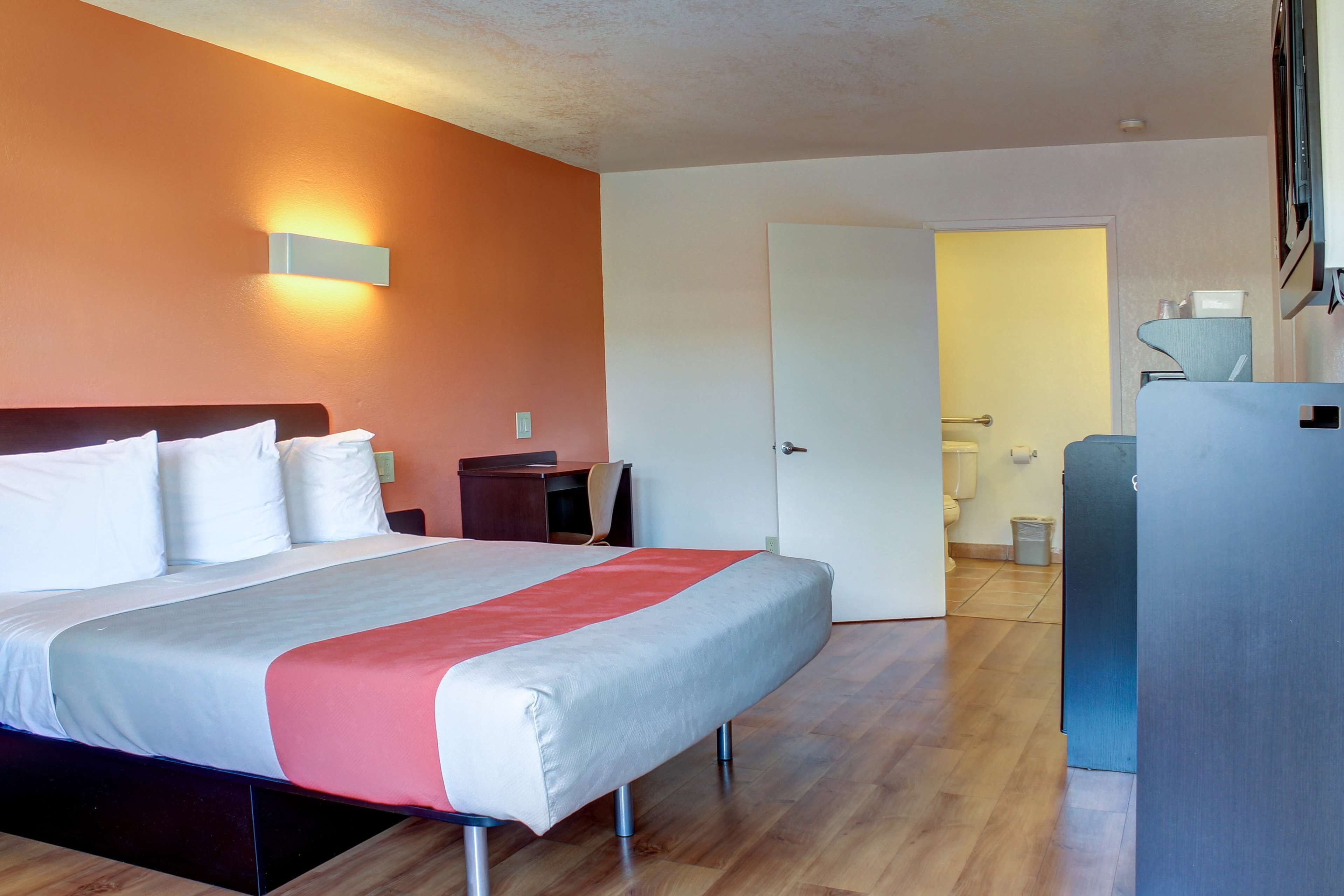 Une chambre d’hôtel avec un lit, un bureau et une salle de bain, visibles à travers une porte ouverte.