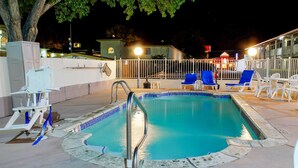 An outdoor swimming pool with a metal ladder, surrounded by white and blue lounge chairs, and a white fence. - Motel 6 Bishop, CA (Bishop)