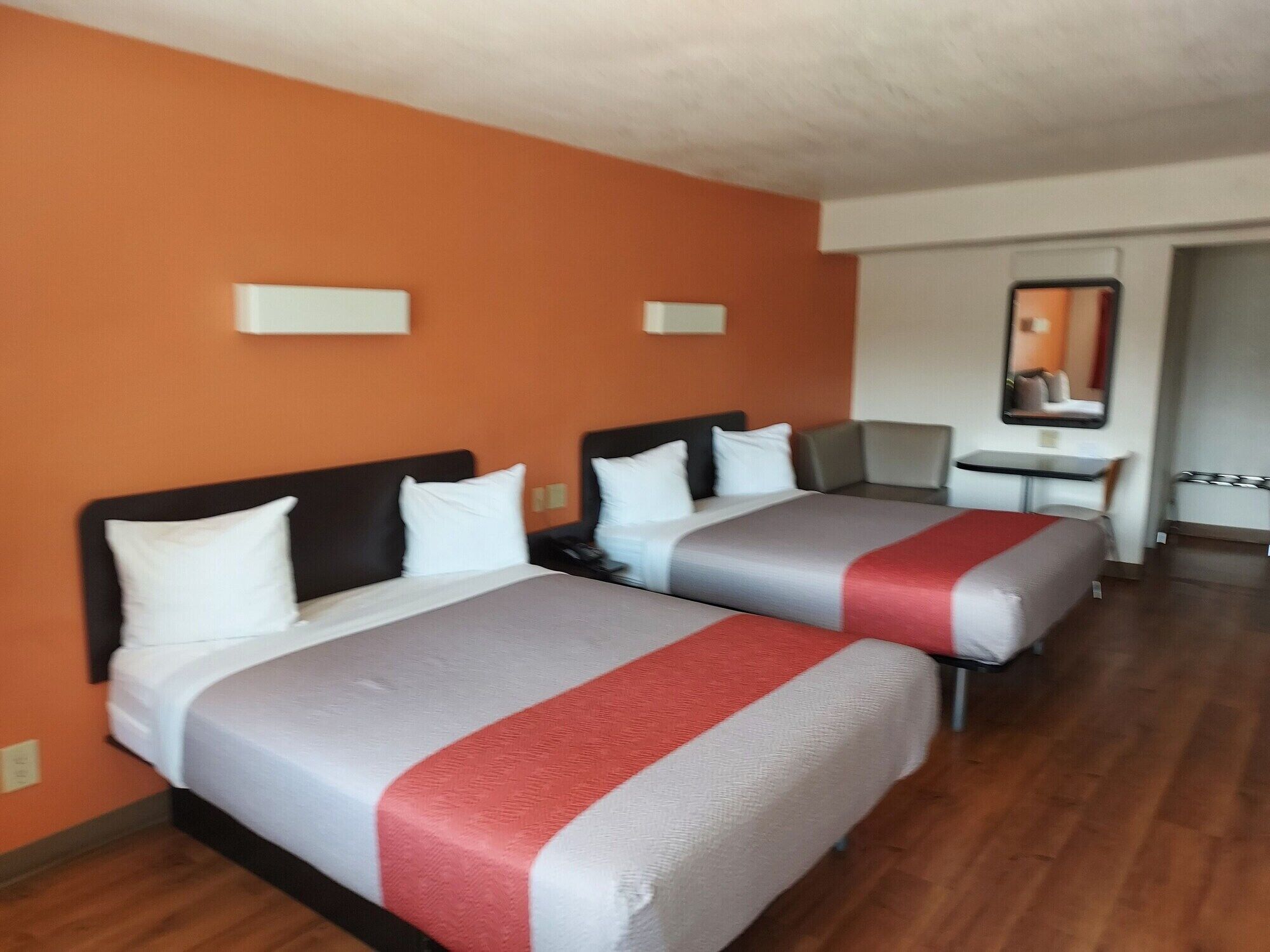 A hotel room with two beds, a small table, and a mirror.