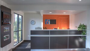 A reception area with a modern design, featuring a reception desk, a clock, and a large window. - Motel 6 Bishop, CA (Bishop)