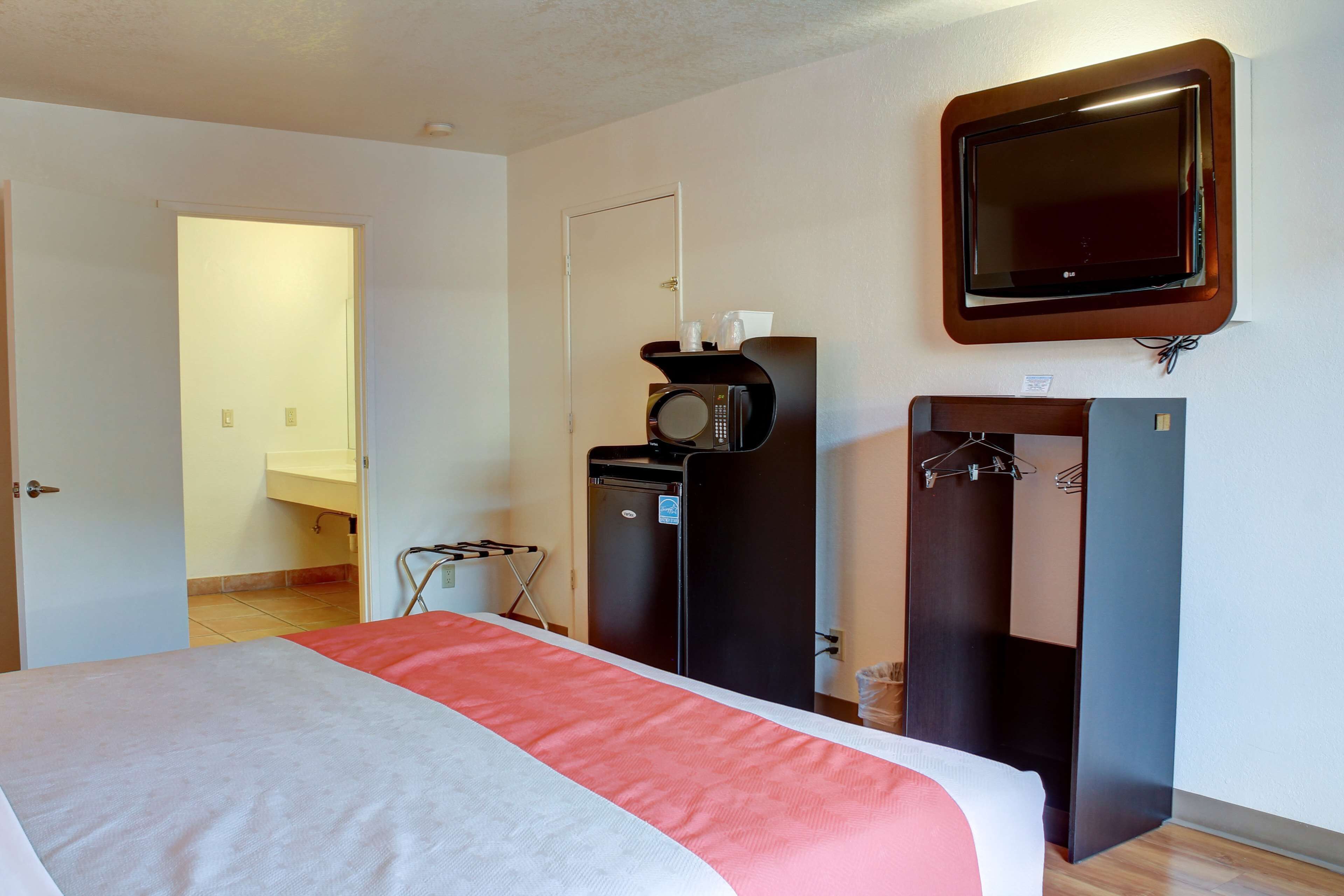 Una habitación de hotel con una cama, televisión instalada en la pared, microondas y un refrigerador pequeño.