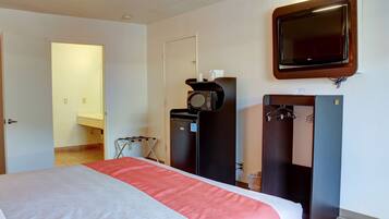 Una habitación de hotel con una cama, televisión instalada en la pared, microondas y un refrigerador pequeño.