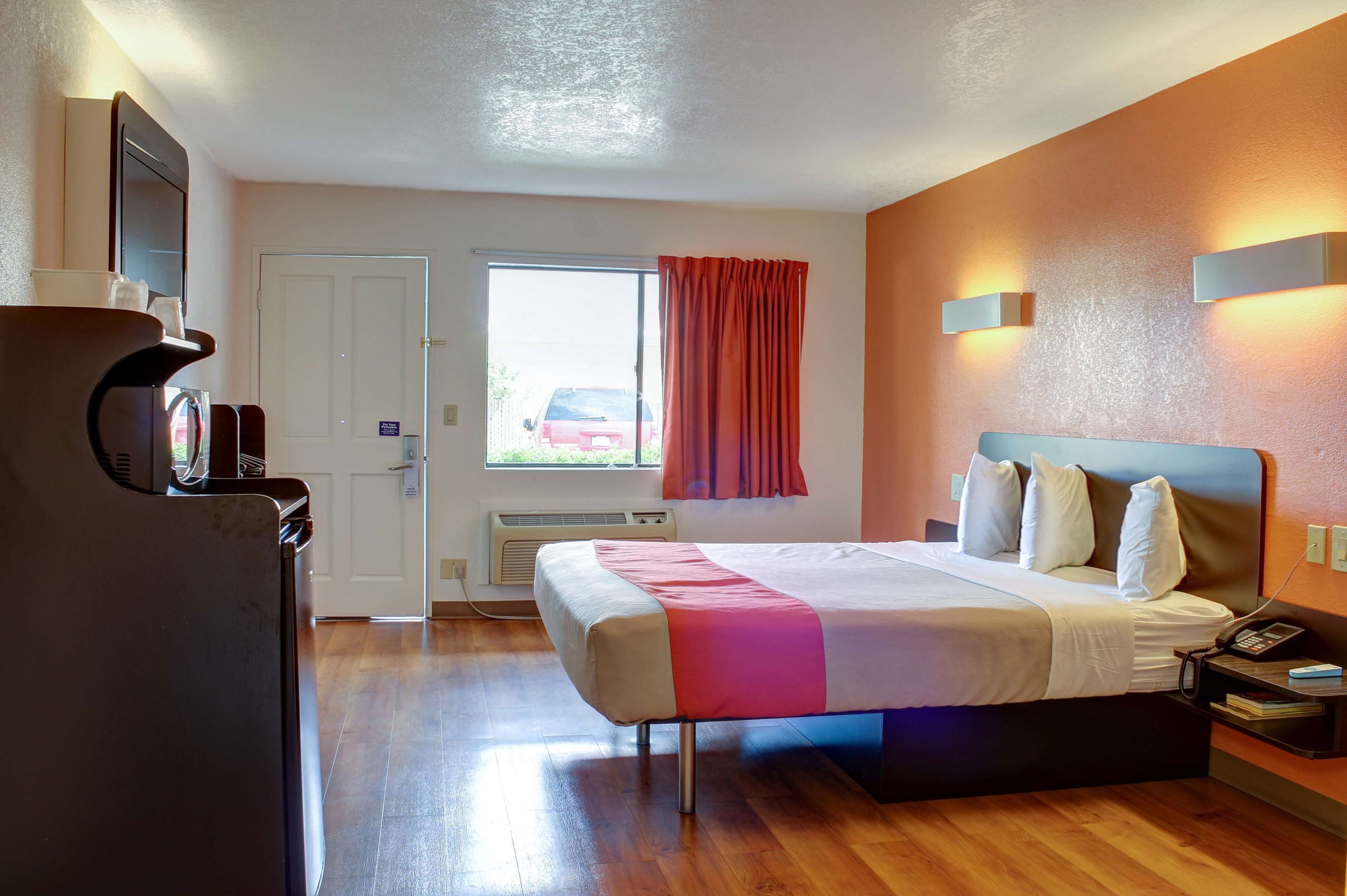 A hotel room with a bed, bedside table, lamp, and a window with curtains.