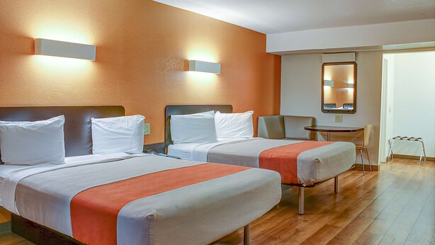 A hotel room with two beds, a small table, a chair, and a mirror on the wall. - Motel 6 Bishop, CA (Bishop)