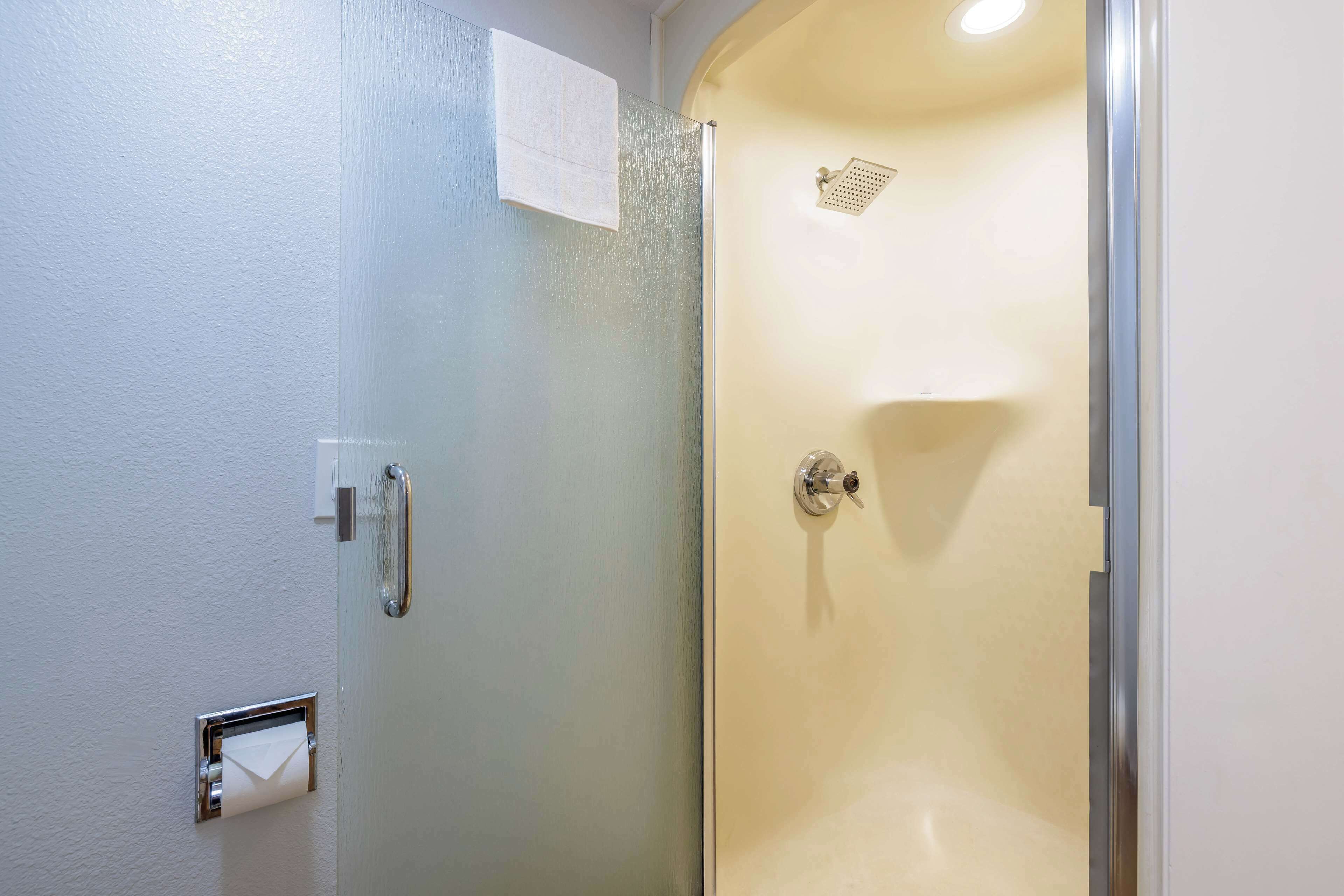 A bathroom with a glass shower enclosure, a towel dispenser, and a paper towel dispenser.