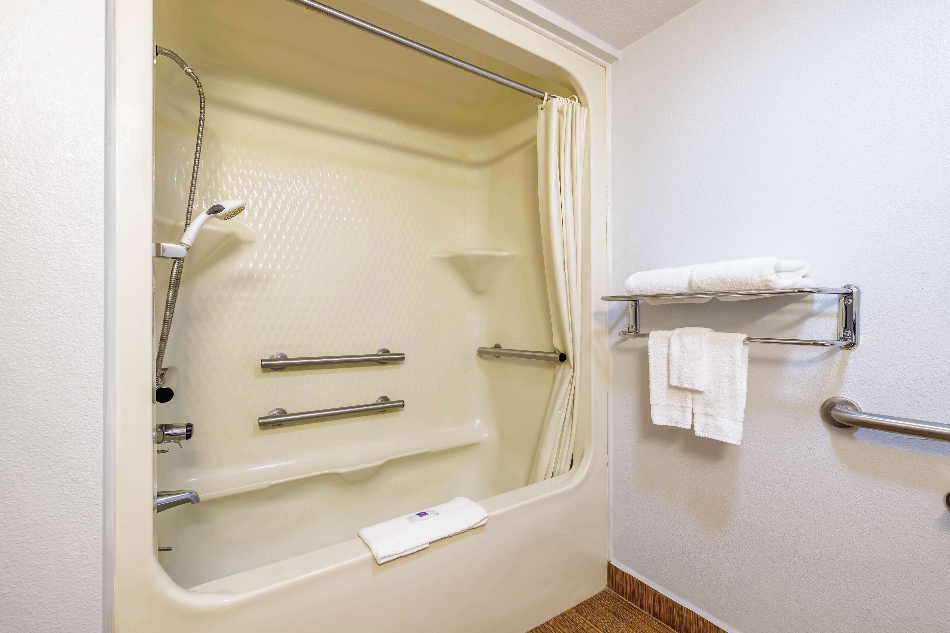 A bathroom with a bathtub, shower, and handrails. There is a towel rack with towels.