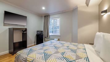 Quarto de hotel com cama, televisão de tela plana na parede, janela com cortinas e ar condicionado integrado.