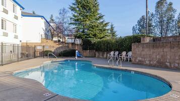 A swimming pool with a clear blue water, surrounded by a paved deck, a brick wall, and a metal fence.