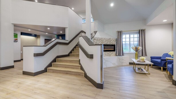 A spacious living area with a wooden staircase, a fireplace, and blue sofas. - Motel 6 Auburn, CA (Auburn)