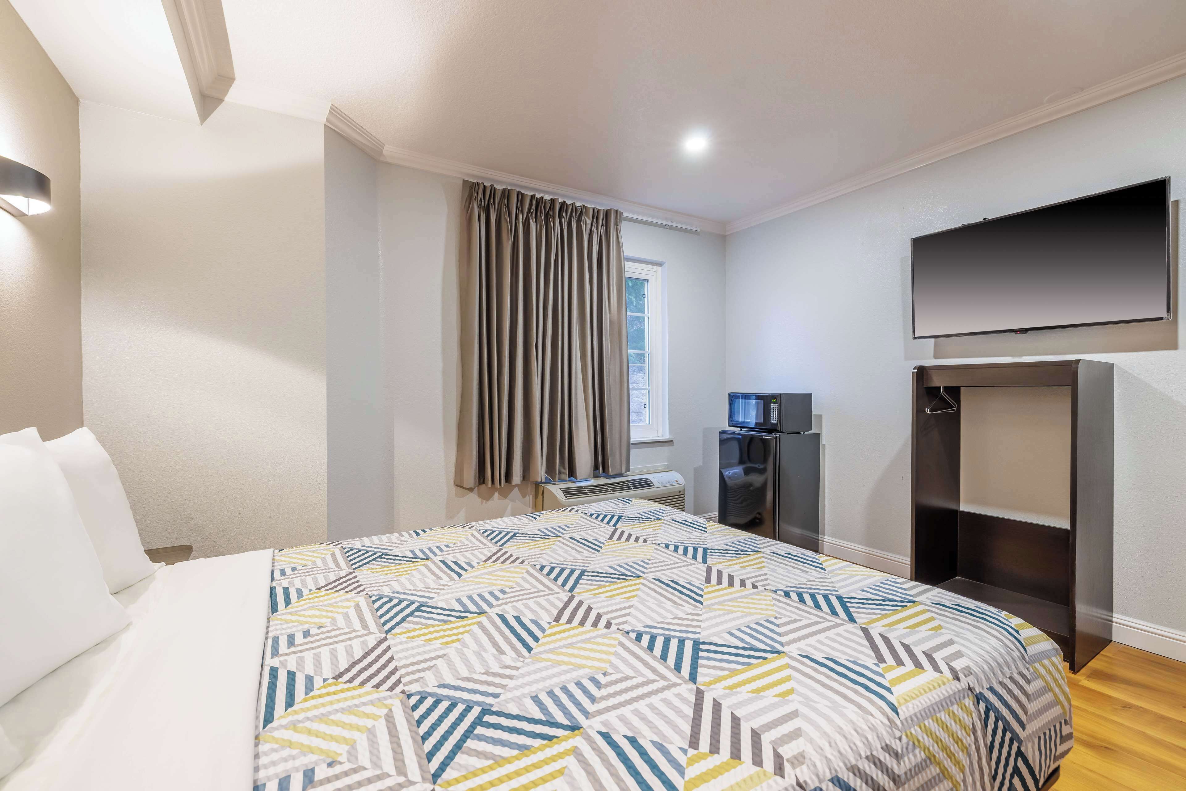Une chambre d’hôtel équipée d’un lit, d’un téléviseur à écran plat fixé au mur, d’une armoire intégrée et d’une fenêtre avec des rideaux.