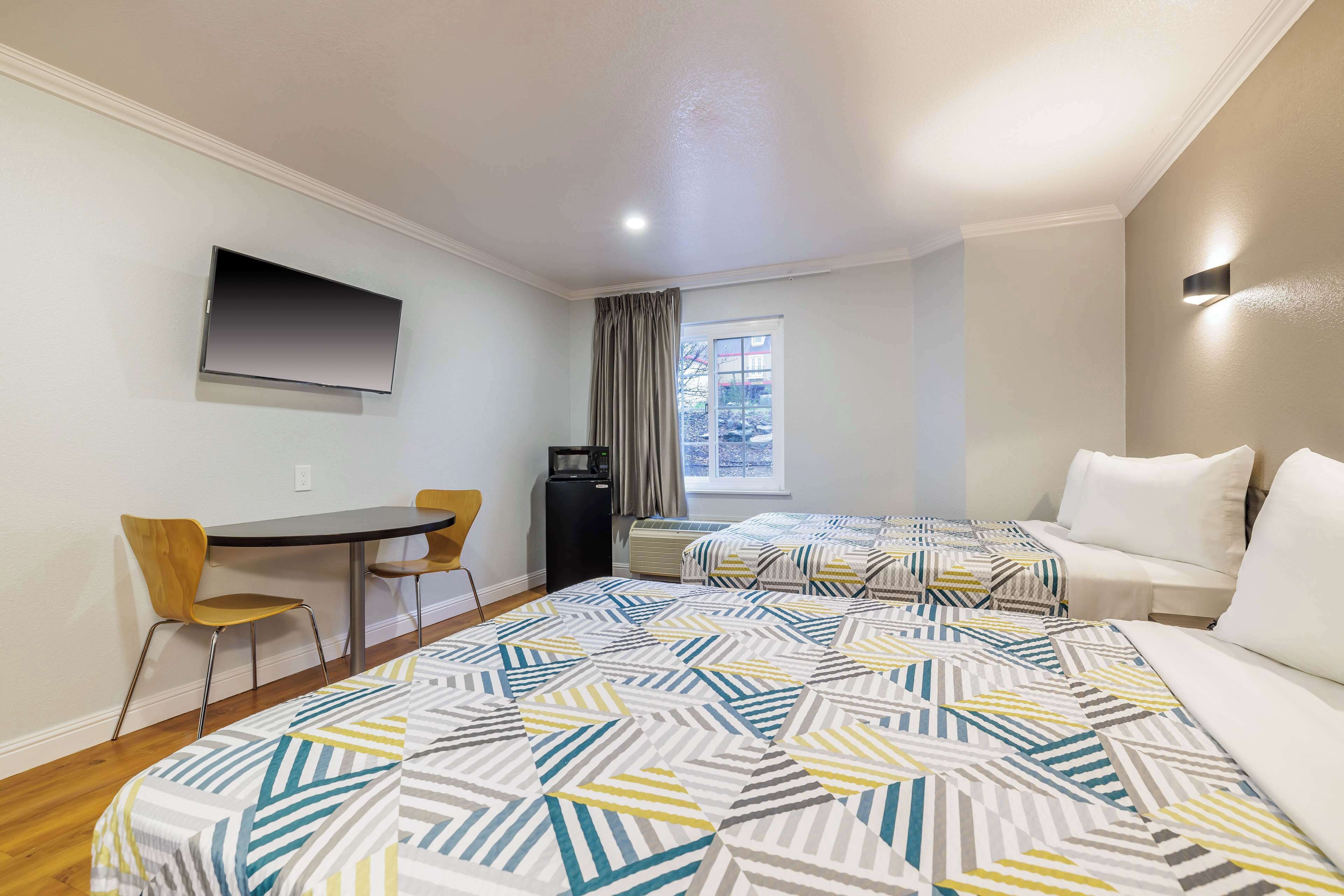 A hotel room with a bed, a desk, a chair, a TV, and a window.