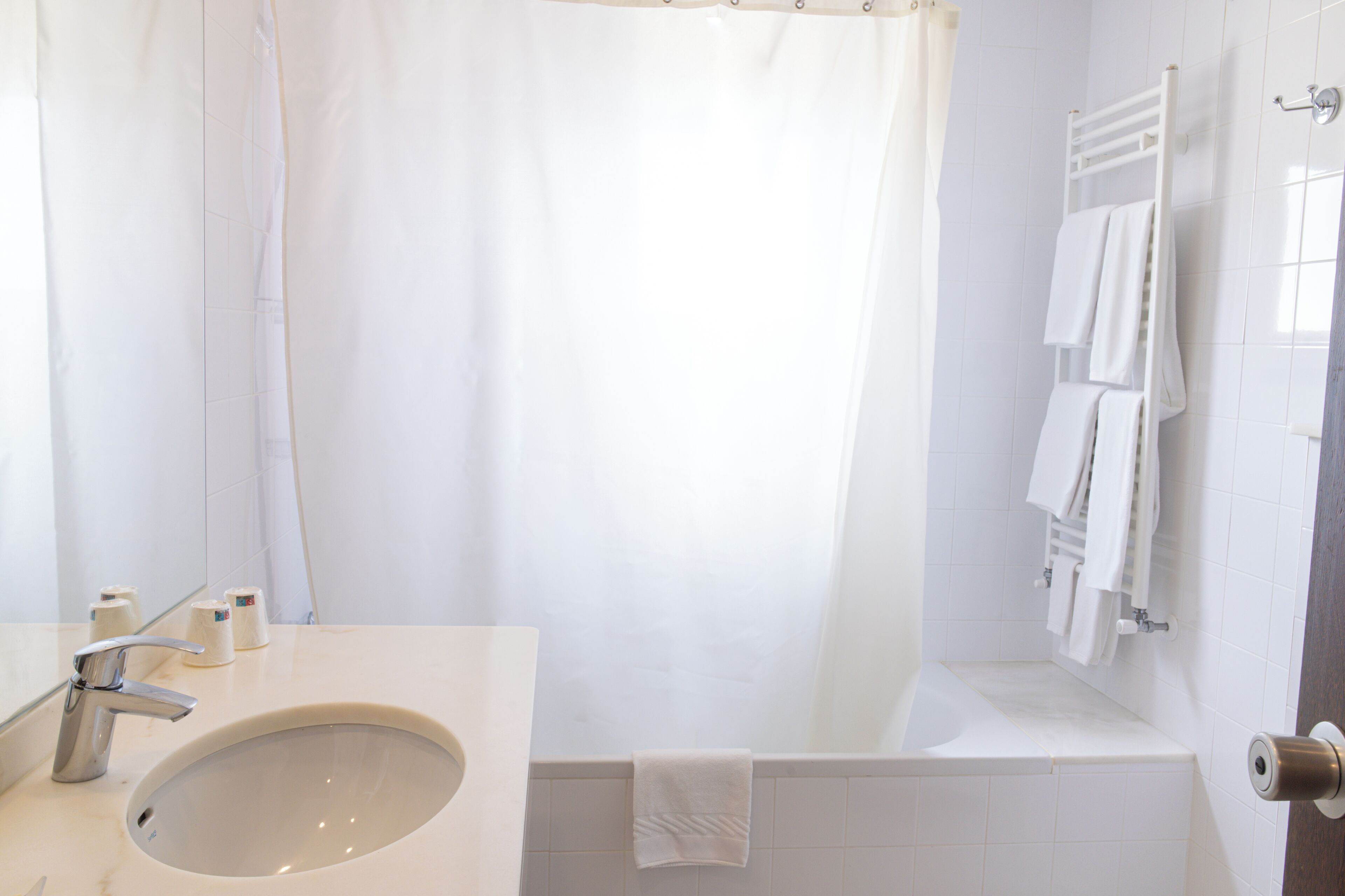 Un baño con lavamanos, espejo, cortina de ducha y toallero con toallas.