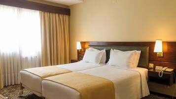 A hotel room with two beds, a wooden headboard, a nightstand with a phone, and a window with curtains.