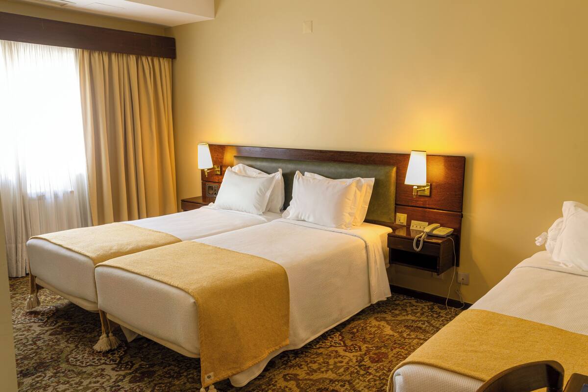 A hotel room with two beds, a nightstand with a phone, and a window with curtains.