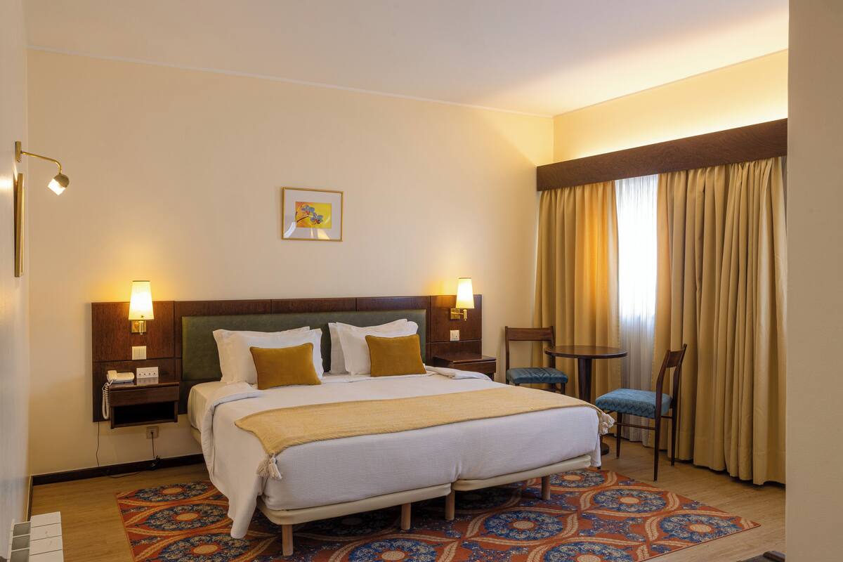 A hotel room with a large bed, two bedside tables, a desk, a chair, and a patterned rug.