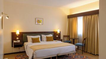 A hotel room with a large bed, two bedside tables, a desk, a chair, and a patterned rug.