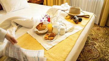 A neatly made bed with a breakfast tray including croissants, orange juice, and coffee, a camera, and a hat on the bed.