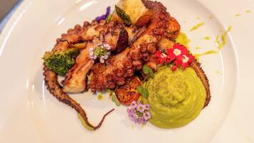 Un plato de comida con pulpo, verduras y una cucharada de salsa verde.