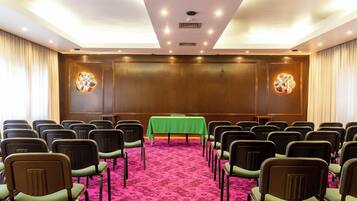 Un salón de conferencias con filas de sillas, una mesa verde y piso alfombrado.
