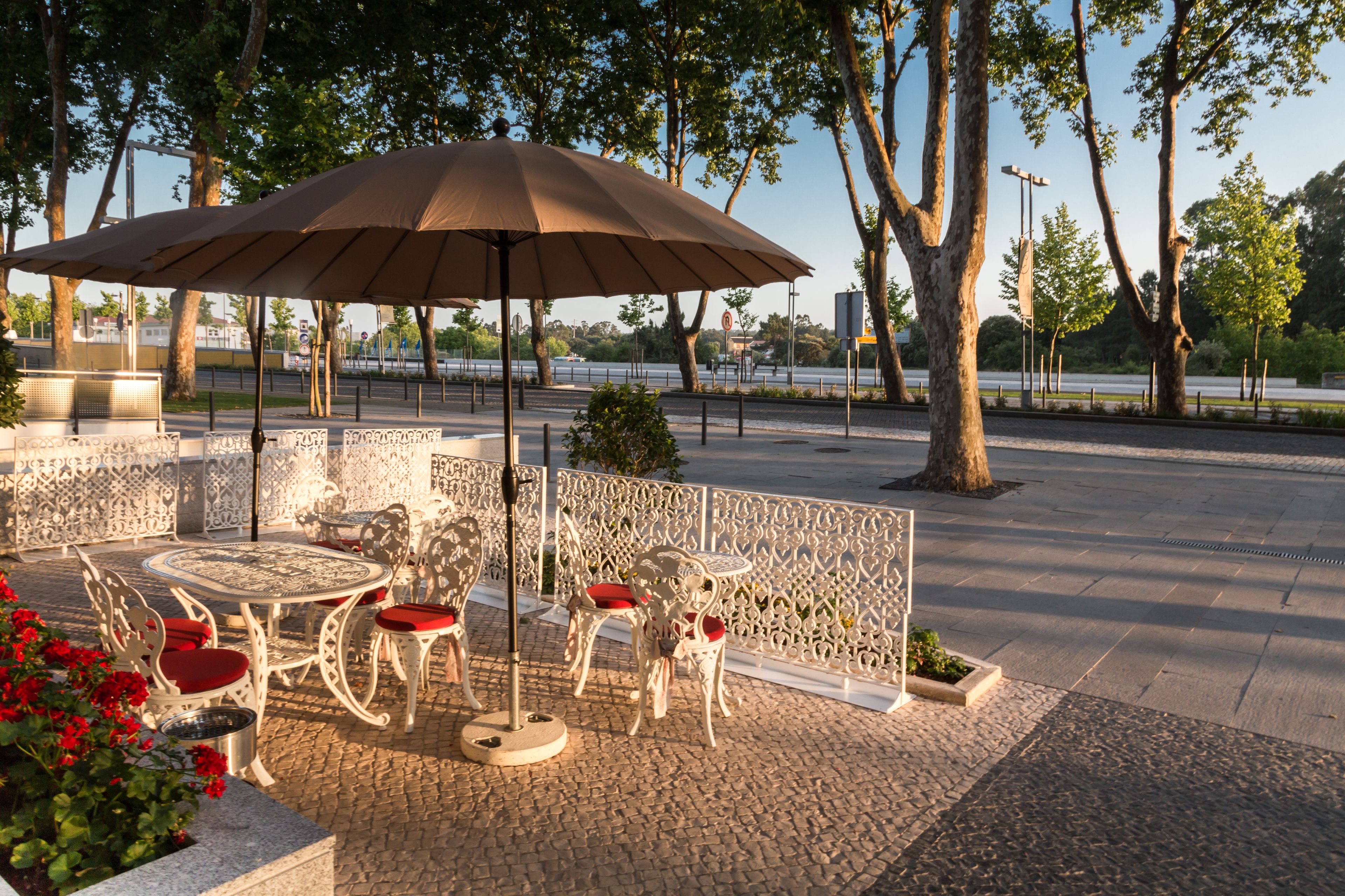 Un patio al aire libre con una mesa redonda y sillas, rodeado por una cerca decorativa y árboles.