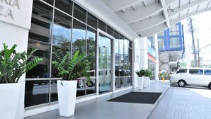 A modern building with large glass windows, white exterior walls, and potted plants. - Astoria Plaza (Pasig)