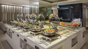 A buffet setup with multiple food stations, including hot and cold dishes, arranged on a white counter with stainless steel serving ware. - Astoria Plaza (Pasig)