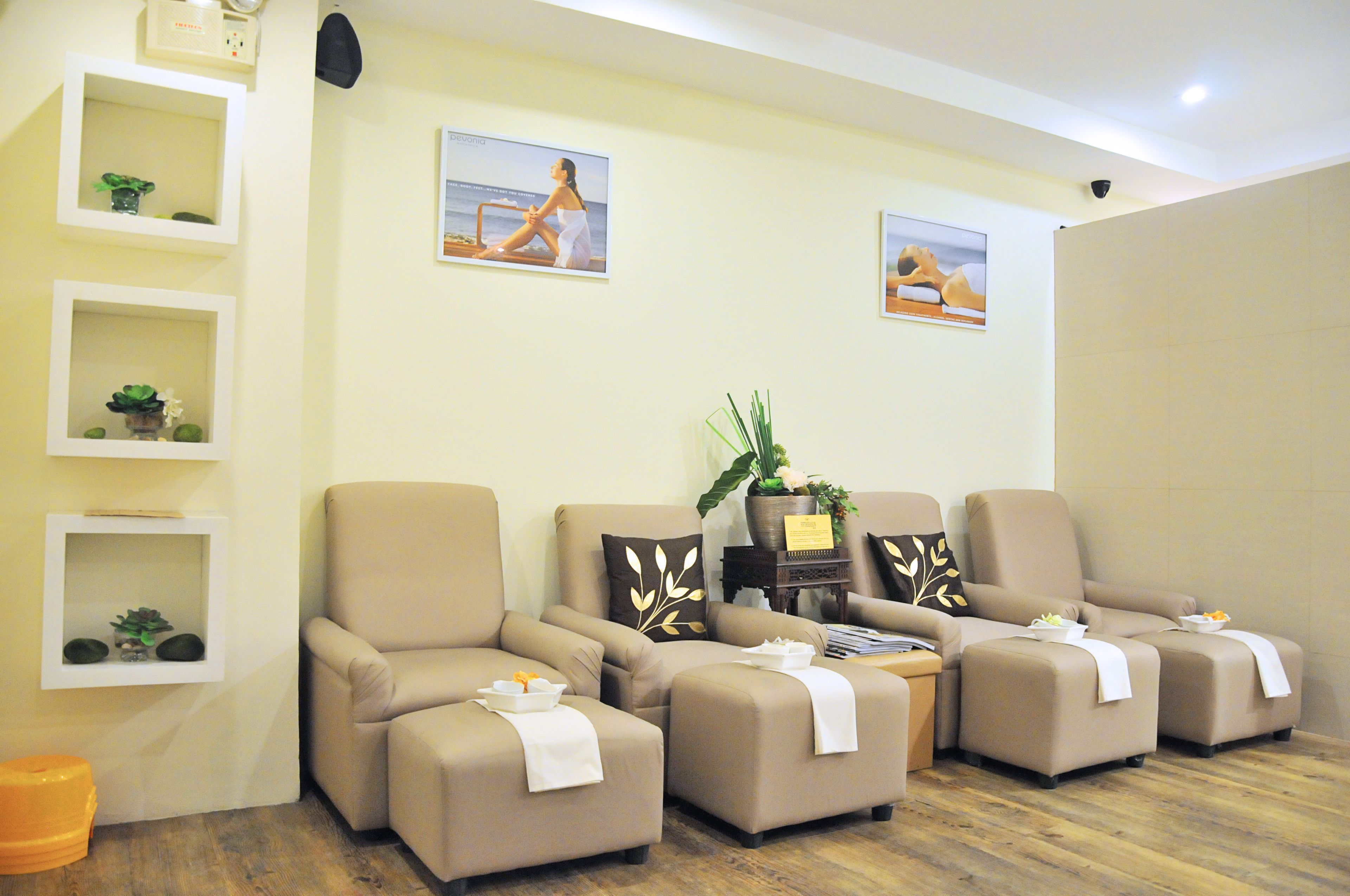 Une salle de spa avec quatre chaises beiges, une petite étagère avec des plantes et deux tableaux encadrés au mur.