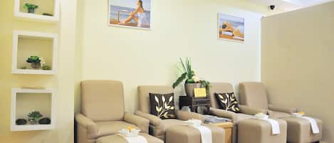 Une salle de spa avec quatre chaises beiges, une petite étagère avec des plantes et deux tableaux encadrés au mur.